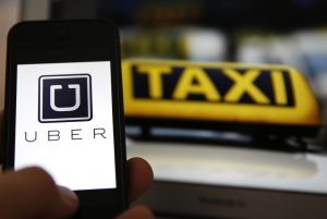 File illustration picture showing the logo of car-sharing service app Uber on a smartphone next to the picture of an official German taxi sign in Frankfurt, September 15, 2014. A Frankfurt court earlier this month instituted a temporary injunction against Uber from offering car-sharing services across Germany. San Francisco-based Uber, which allows users to summon taxi-like services on their smartphones, offers two main services, Uber, its classic low-cost, limousine pick-up service, and Uberpop, a newer ride-sharing service, which connects private drivers to passengers - an established practice in Germany that nonetheless operates in a legal grey area of rules governing commercial transportation. REUTERS/Kai Pfaffenbach/Files (GERMANY - Tags: BUSINESS EMPLOYMENT CRIME LAW TRANSPORT)